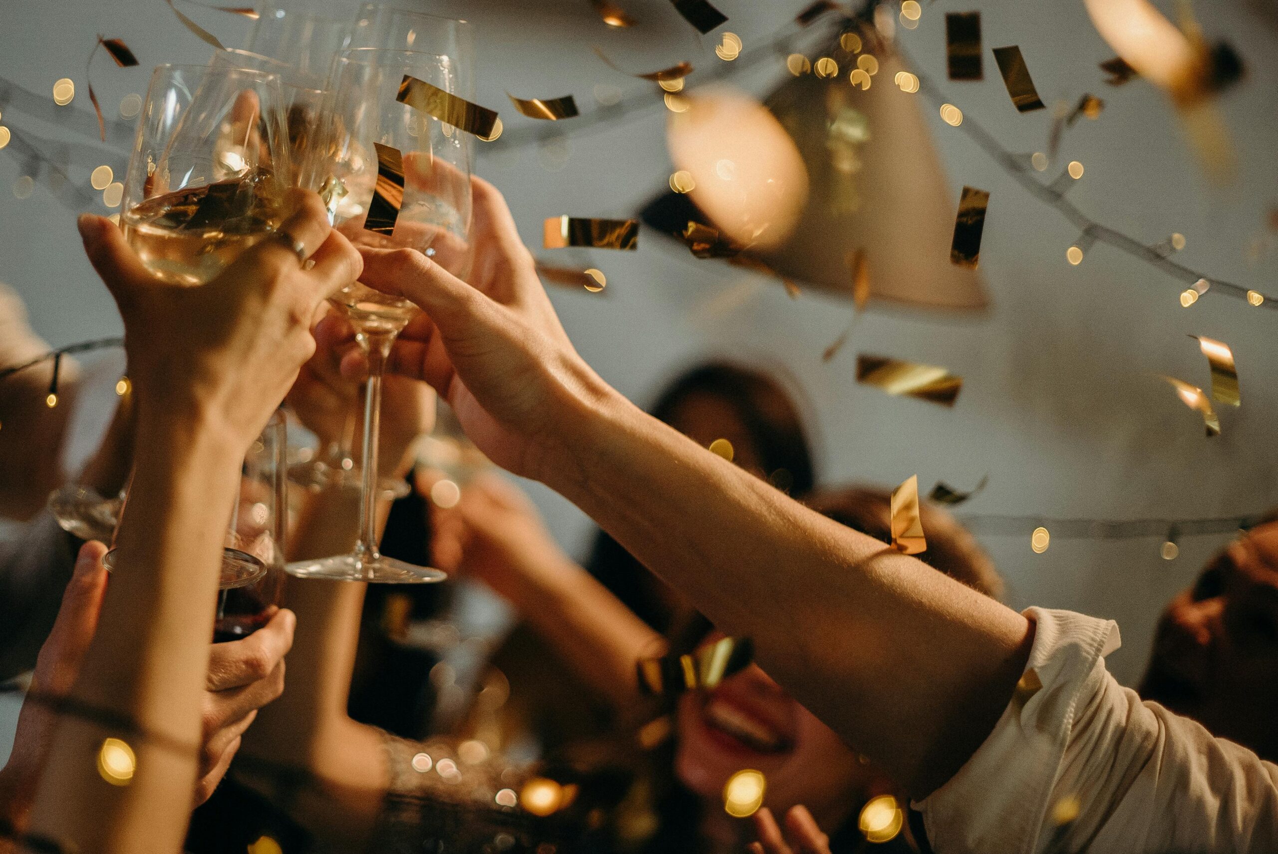 A lively indoor party scene with people toasting champagne glasses amid confetti and warm lights.