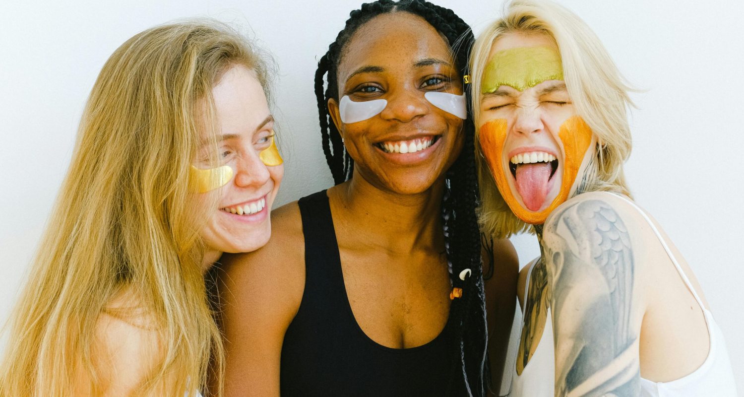 Three diverse women having fun with colorful skincare masks, embodying friendship and joy.