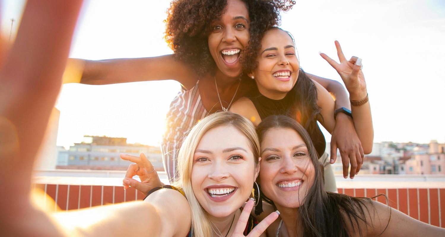 Cheerful friends capturing a fun selfie on a rooftop during sunset, enjoying a positive and trendy moment.