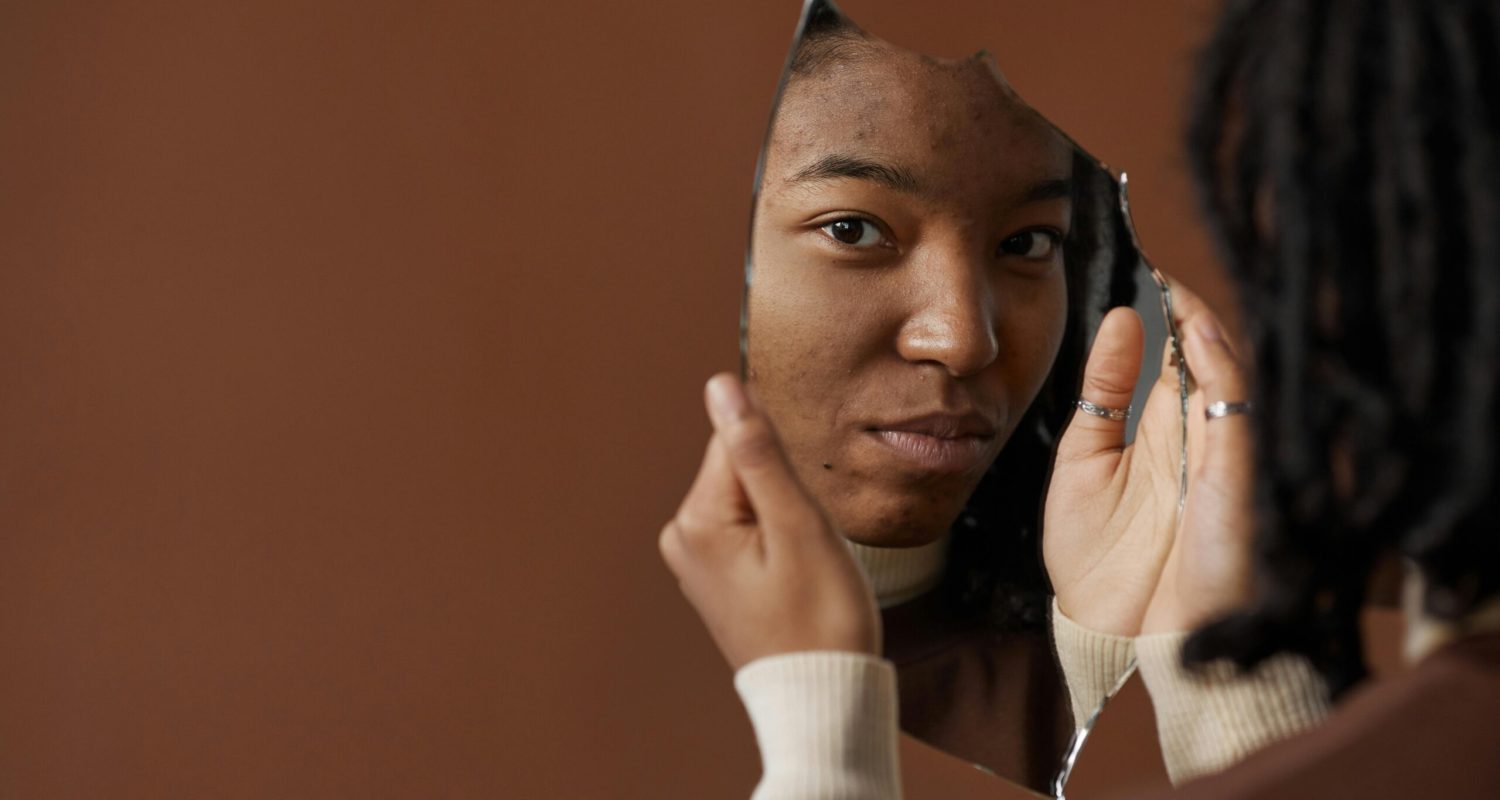 A woman holding and looking into a broken mirror, reflecting on self image and identity.